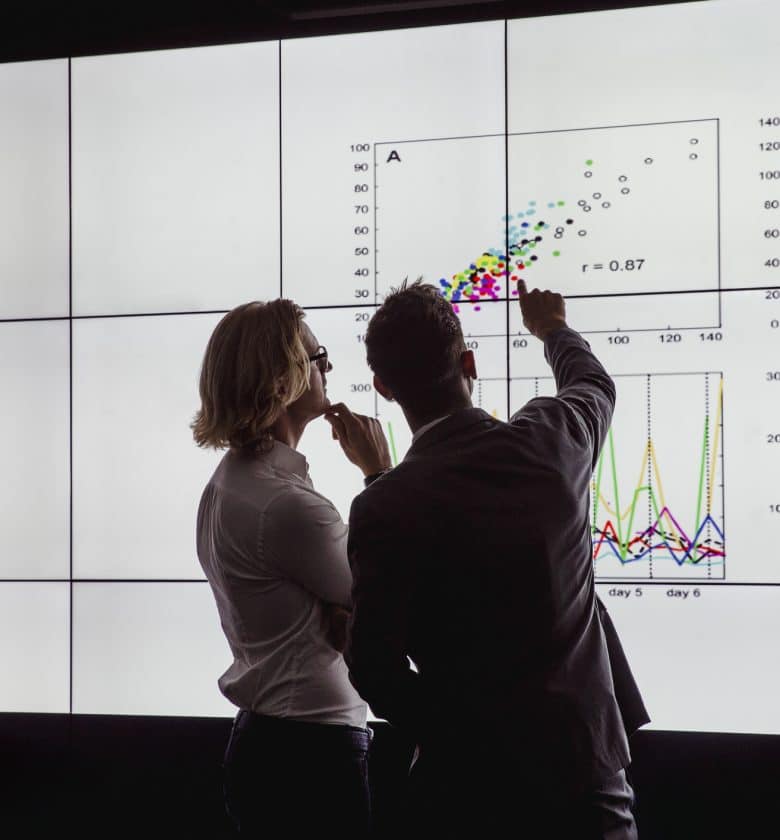 Two people examining charts on a large monitor