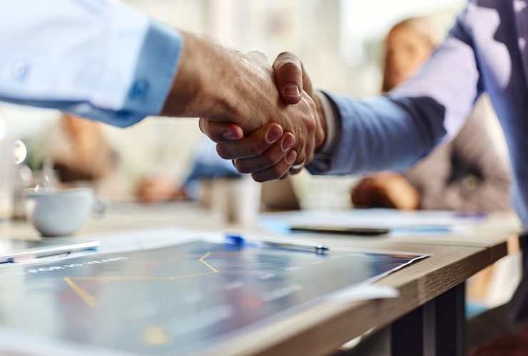 Two people shaking hands over a table during a business meeting