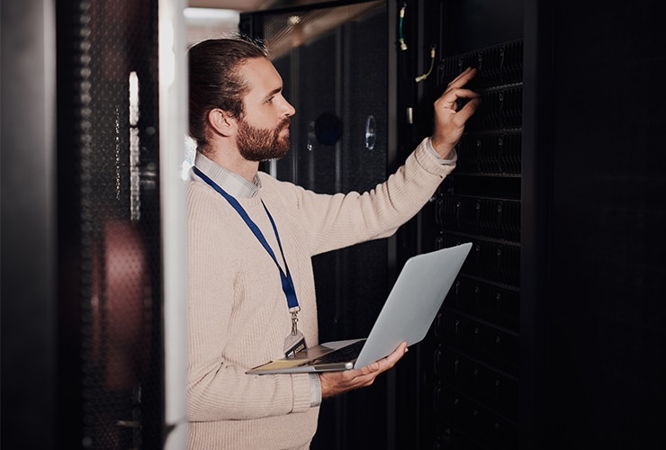 A man holding a laptop in a server room