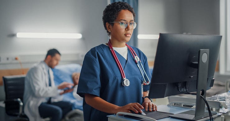 A female nurse in scrubs typing on a computer